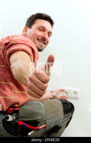 Electrician installing a power socket giving the thumbs-up sign - focus on thumb Stock Photo