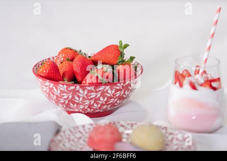 Tempting bowl of strawberries surrounded by out of focus sweets on a light background: Selective focus and close up. Fruits and desserts concept. Stock Photo