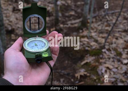 A hand is holding a prismatic compass and raising it for navigational use on a hiking trail in this point-of-view image. Stock Photo