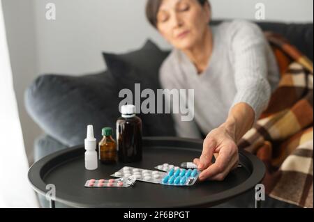 Tablets, pills and different treatment remedies on the table near couch, a senior woman in out of focus taking a one Stock Photo