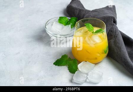 A glass of orange cocktail with mint and ice cubes on a light gray background with a linen napkin. Stock Photo