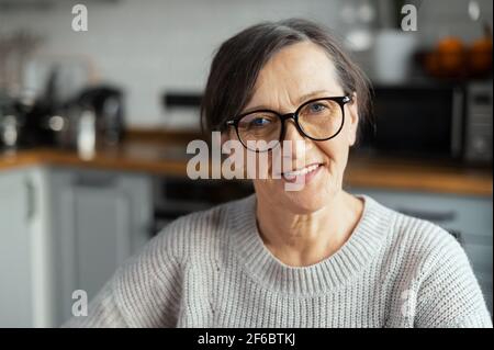 Close-up portrait of contemporary senior woman wearing stylish eyewear looks at the camera and smiles, video meeting with an elderly female Stock Photo