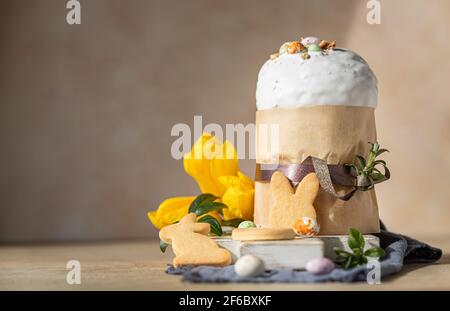 Easter composition with traditional Orthodox sweet bread. Kulich decorated with meringue icing, candy shaped eggs, easter cookies and tulip. Selective Stock Photo