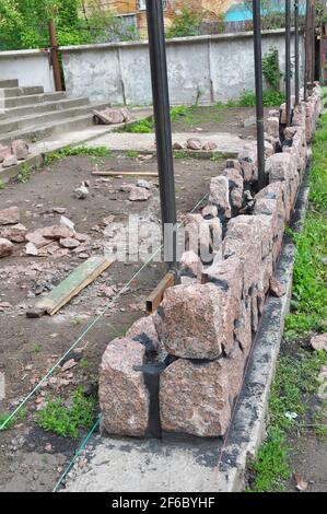 Building Granite Stone Fence with Design Decorative Cracked Real Stone Wall Surface. Stock Photo