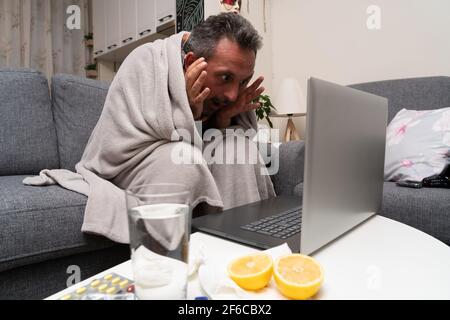 Shocked adult man feeling unwell looking at laptop screen working remote online from home as pandemic concept having cold flu sars covid19 symptoms at Stock Photo