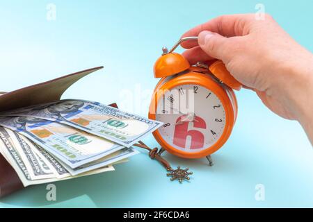 Concept of vacation, travel, adventure. A hand holds an orange alarm clock and dollars in an open wallet on a blue background. Time to relax concept Stock Photo