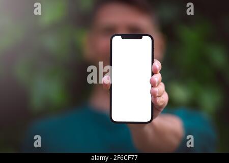 Modern smartphone mockup, blank screen. Young man showing or holding his phone with blank space outdoors on a green background Stock Photo