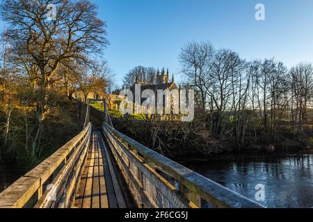 The Boat Weil Wooden Suspension Bridge over the Water of Ken, with Dalry Parish Church in the background, at St.John's town of Dalry, Scotland Stock Photo