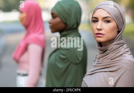 Side-View Group Portrait Of Three Diverse Muslim Women Posing Outside Stock Photo