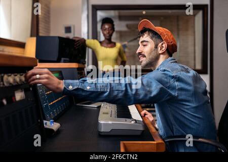 Stock photo of happy black woman in music studio and male producer using electronic piano keyboard. Stock Photo
