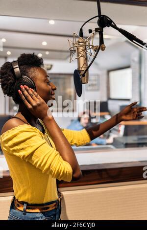 Stock photo of beautiful black woman with headphones using microphone in music studio. Stock Photo