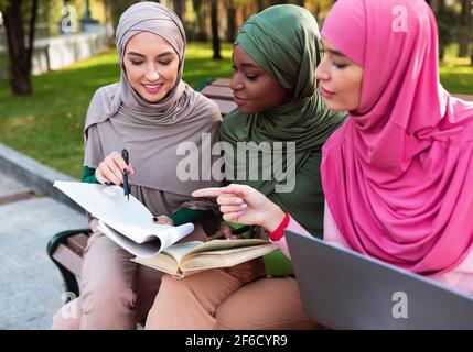 Three Muslim Females Students Learning Together Sitting On Bench Outside Stock Photo