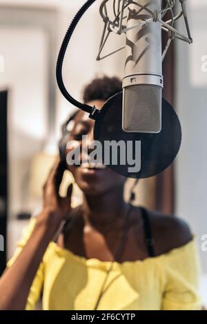 Stock photo of beautiful black woman singing and using microphone in music studio. Stock Photo