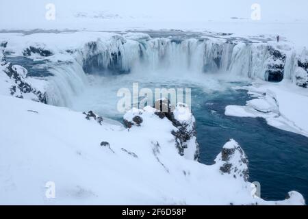 Goðafoss waterfall complex with a photographer near to the edge during winter conditions showing the 12 metre drop full of ice features on the  river