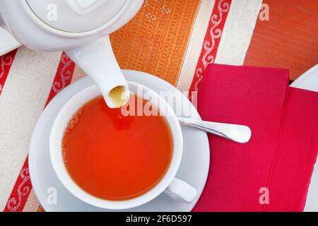 Tea from ceramic white teapot is poured into cup. Tea in cafe. Stock Photo