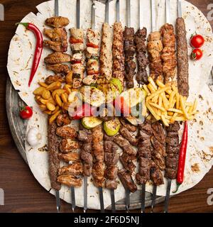 Assorted delicious grilled meat on skewers with vegetables and French fries on pita. Top view Stock Photo