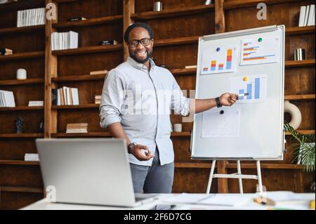 Male black entrepreneur has online conference showing financial graphics diagrams, makes deal remotely, works with interactive whiteboard, discussing with business partner via video call, presentation Stock Photo