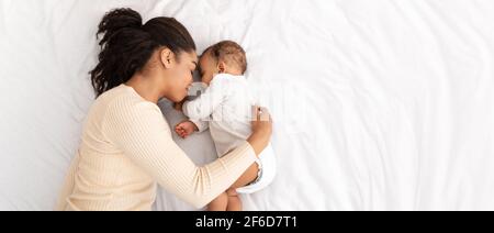 African Mother Hugging Sleeping Baby Lying In Bed Indoor, High-Angle Stock Photo