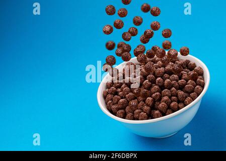 Chocolate Corn balls falling in bowl over blue background Stock Photo