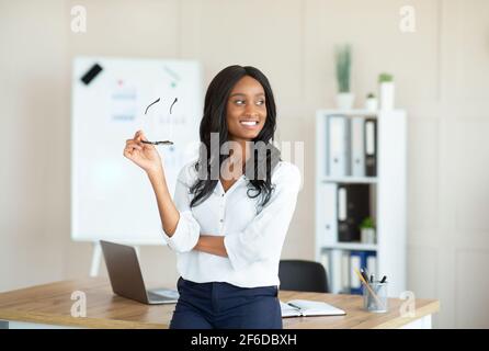 Portrait of positive female manager in formal clothes holding glasses at modern office Stock Photo