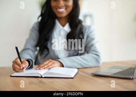 Unrecognizable black female secretary writing down info during online business meeting at workplace, selective focus Stock Photo