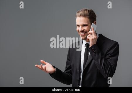 joyful manager pointing with hand while talking on cellphone isolated on grey Stock Photo