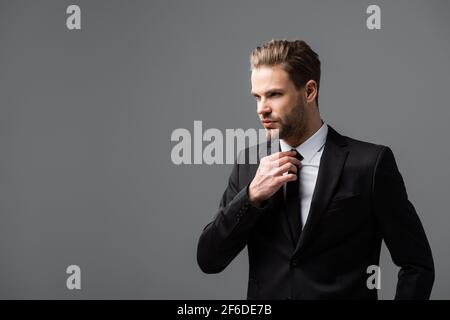 successful businessman looking away while touching tie isolated on grey Stock Photo