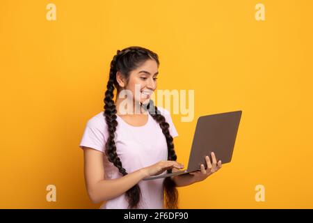 Smiling young indian lady holding and using laptop Stock Photo
