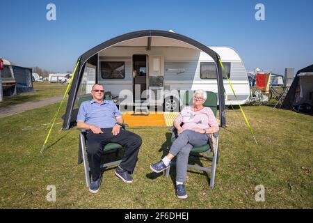 Hooksiel, Germany. 31st Mar, 2021. The permanent campers Karl-Heinz and  Anna from Herford are sitting in front of their caravan on the camping site  of Hooksiel, where they have planned their stay