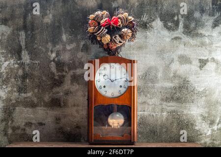 Heart shape wreath made from dried fruits placed over an vintage wood pendulum clock which is leaning against the cement wall. Concept of "There's alw Stock Photo