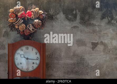 Heart shape wreath made from dried fruits placed over an vintage wood pendulum clock which is leaning against the cement wall. Concept of "There's alw Stock Photo