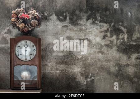 Heart shape wreath made from dried fruits placed over an vintage wood pendulum clock which is leaning against the cement wall. Concept of "There's alw Stock Photo