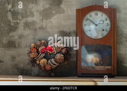 Heart shape wreath made from dried fruits placed with vintage wood pendulum clock which is leaning against the cement wall. Concept of "There's always Stock Photo