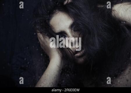 Dark witch behind the wet glass Stock Photo