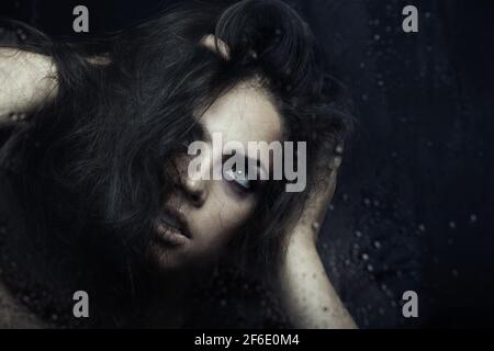 Dark witch behind the wet glass Stock Photo