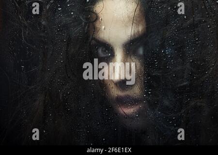 Dark witch behind the wet glass Stock Photo