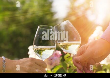 Couple romantically celebrate outdoors with glasses of white wine, proclaim toast People having dinner in a home garden in summer sunlight. Stock Photo