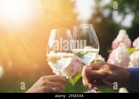 Couple romantically celebrate outdoors with glasses of white wine, proclaim toast People having dinner in a home garden in summer sunlight. Stock Photo
