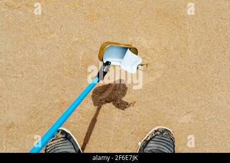 closeup of a man, seen from above, collecting a used food can, with a reach extender, on the wet sand of a beach, as an action to clean up the natural Stock Photo