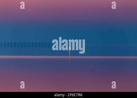 Warning Light on End of Cold War Defence Boom at Shoeburyness taken before Dawn with Deep Tones of Red and Blue with Light Reflected on Calm Sea Stock Photo