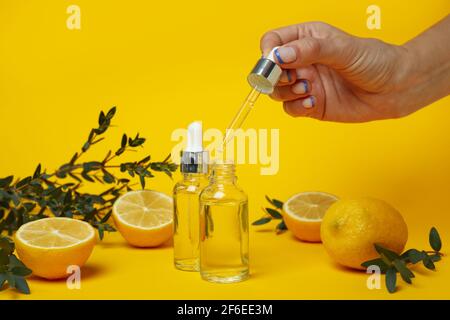 Female hand dripping lemon essential oil from a pipette on a yellow background, natural cosmetics concept Stock Photo