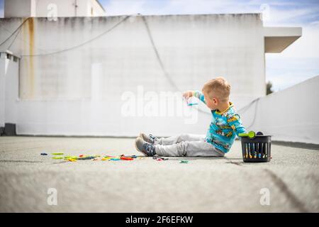 Small boy playing with colorful clothes pegs on the rooftop during the lockdown in the city Stock Photo