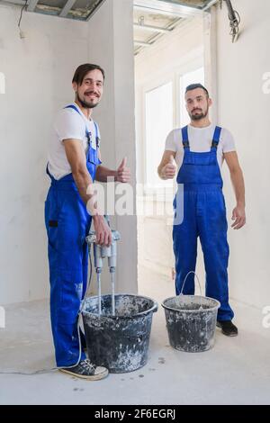 Two construction workers in blue uniform prepare cement in a bucket Stock Photo
