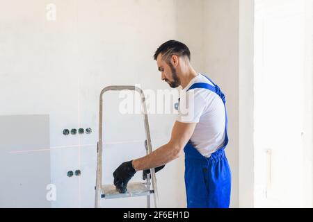 A builder in overalls marks the wall using a laser level Stock Photo