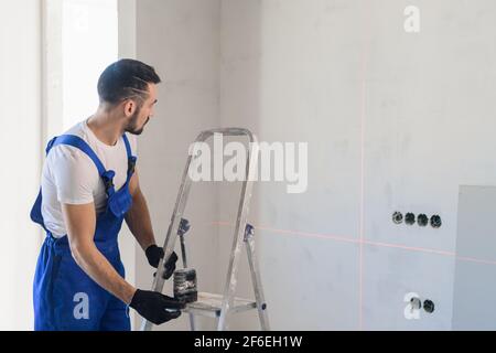 A man in uniform uses an electronic ruler to mark the wall Stock Photo