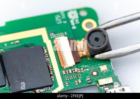 Fix the phone.A technician or master repairs a mobile phone, he installs and changes the camera in the motherboard. Hands, gloves, macro Stock Photo