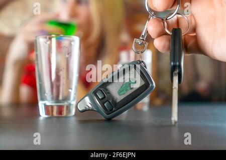 Man's hand holds the car keys in close-up against the background of a stack of vodka and a girl. Concept of drunk driving Stock Photo