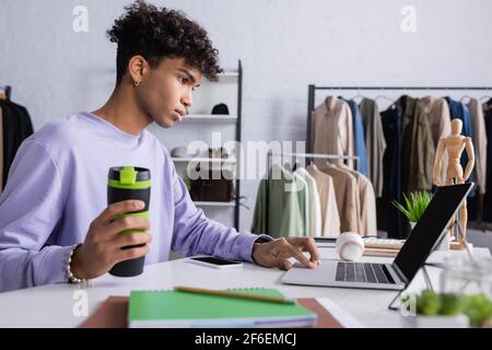 African american showroom owner holding thermo cup and using laptop Stock Photo