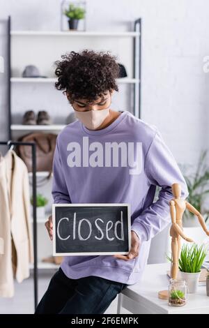African american showroom owner in protective mask looking at chalkboard with closed lettering Stock Photo