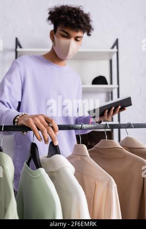 Clothes on hangers near african american owner of showroom with pen and notebook on blurred background Stock Photo